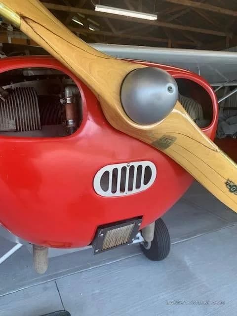 A close-up view of the red engine cowling and wooden propeller of the Aeronca L-16 aircraft.