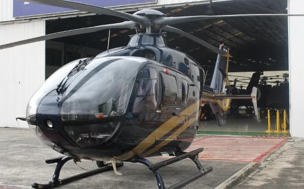 Front view of a dark blue and gold helicopter parked in front of a hangar.