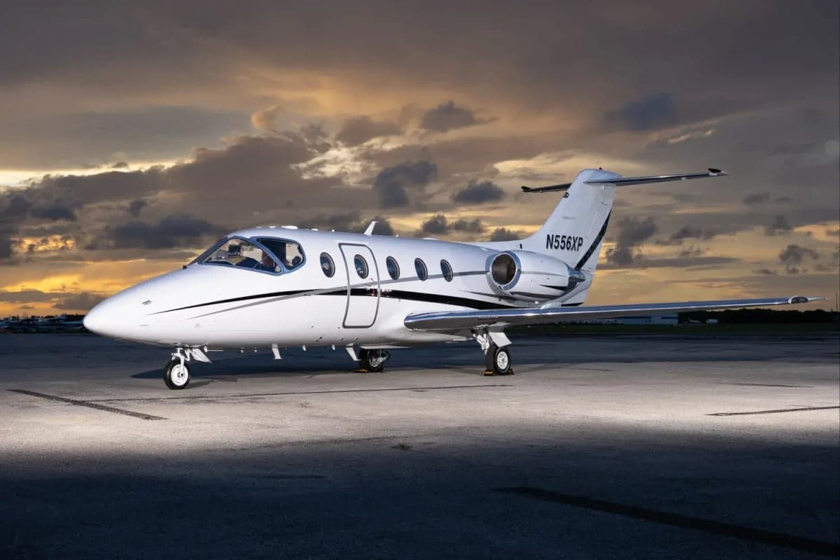 A white Learjet sits on the tarmac in the evening light.