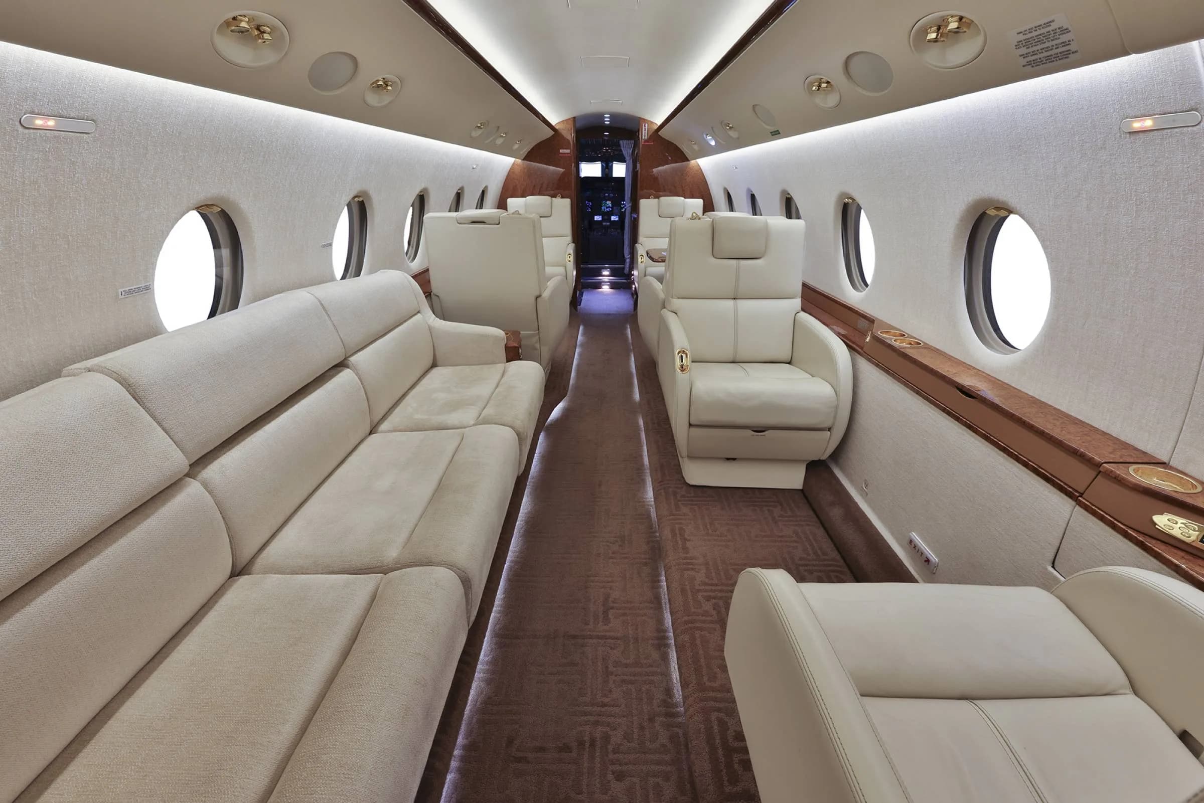 Interior view of a Gulfstream jet with cream-colored leather seats and wood trim.