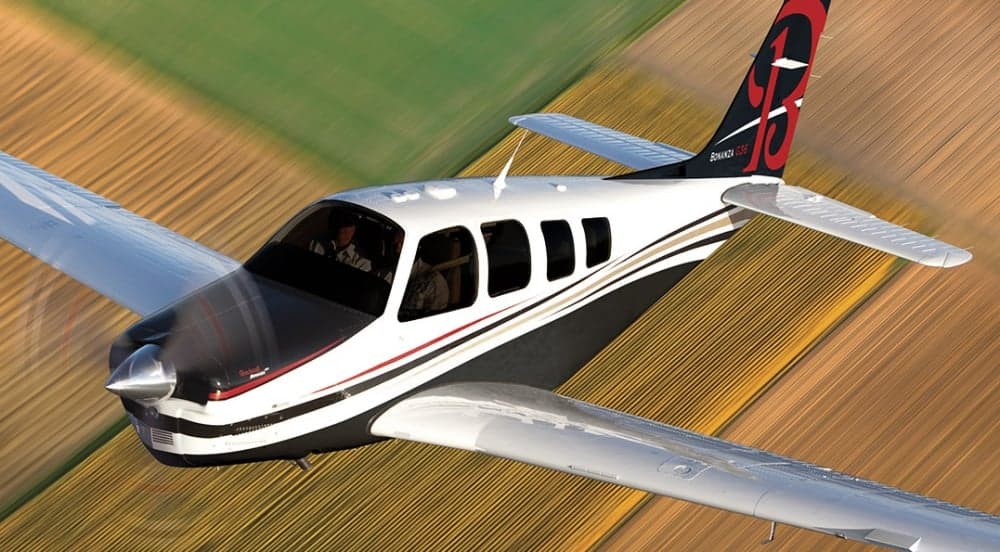 A Bonanza G36 aircraft in flight over a rural landscape.