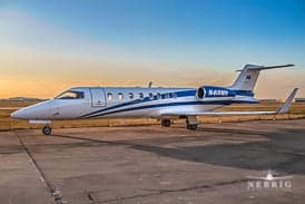A white and blue Learjet business jet, registration N418WB, parked on an airfield at sunset.