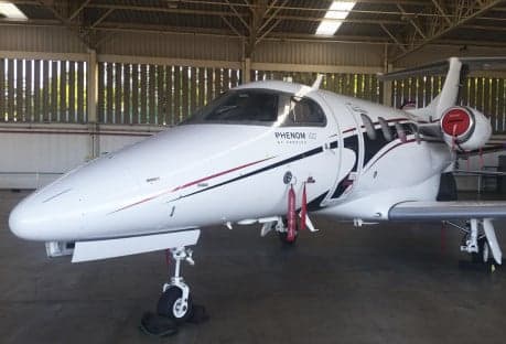 A Phenom 100 aircraft on the runway with a black, white, and orange paint scheme.