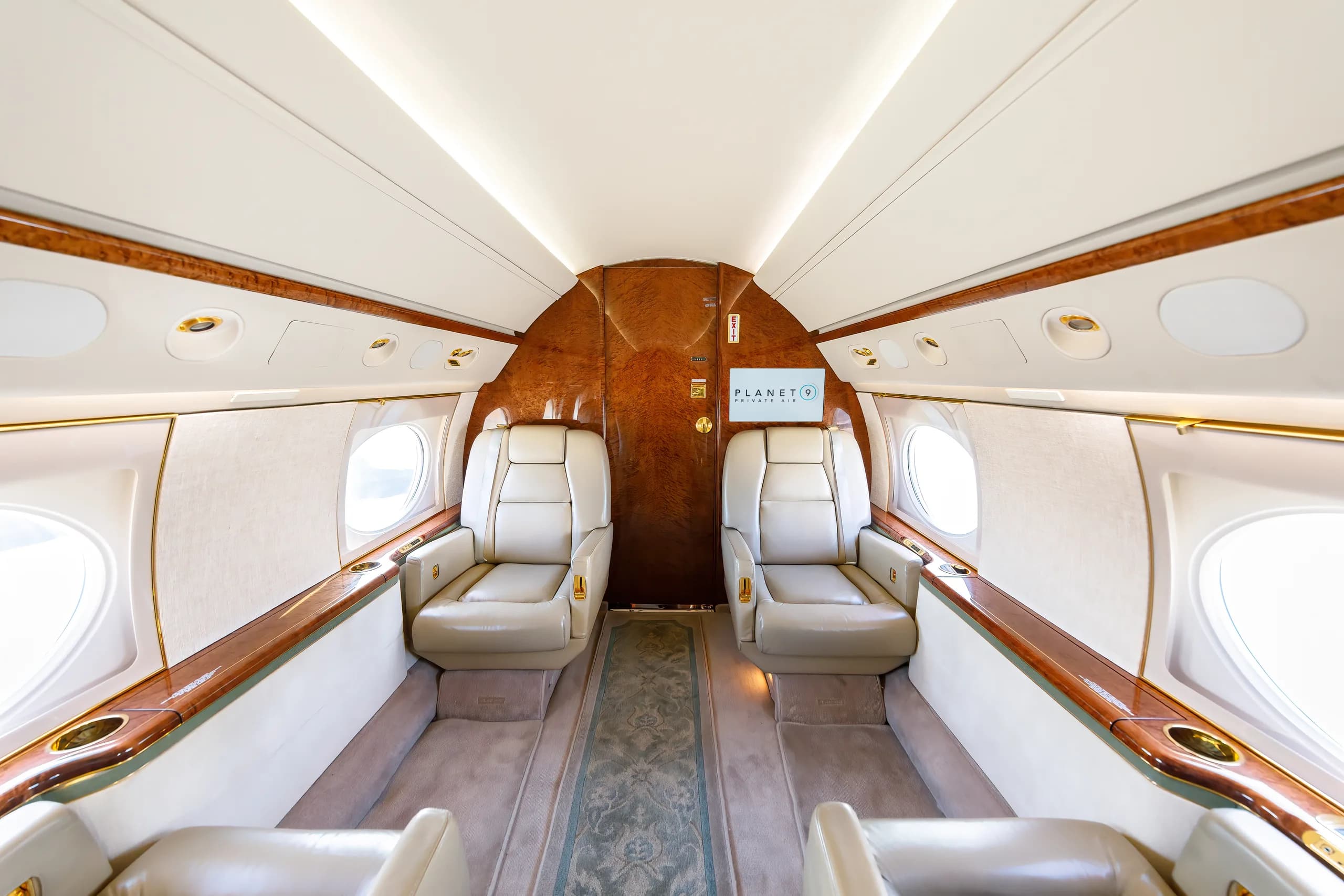 An aircraft cabin interior featuring two light leather seats facing each other, with wood paneling and a screen displaying the "PLANET 9" logo.
