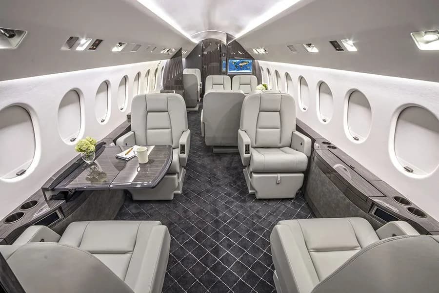 The luxurious cabin interior of a private jet with light grey leather seats and a dark patterned carpet.