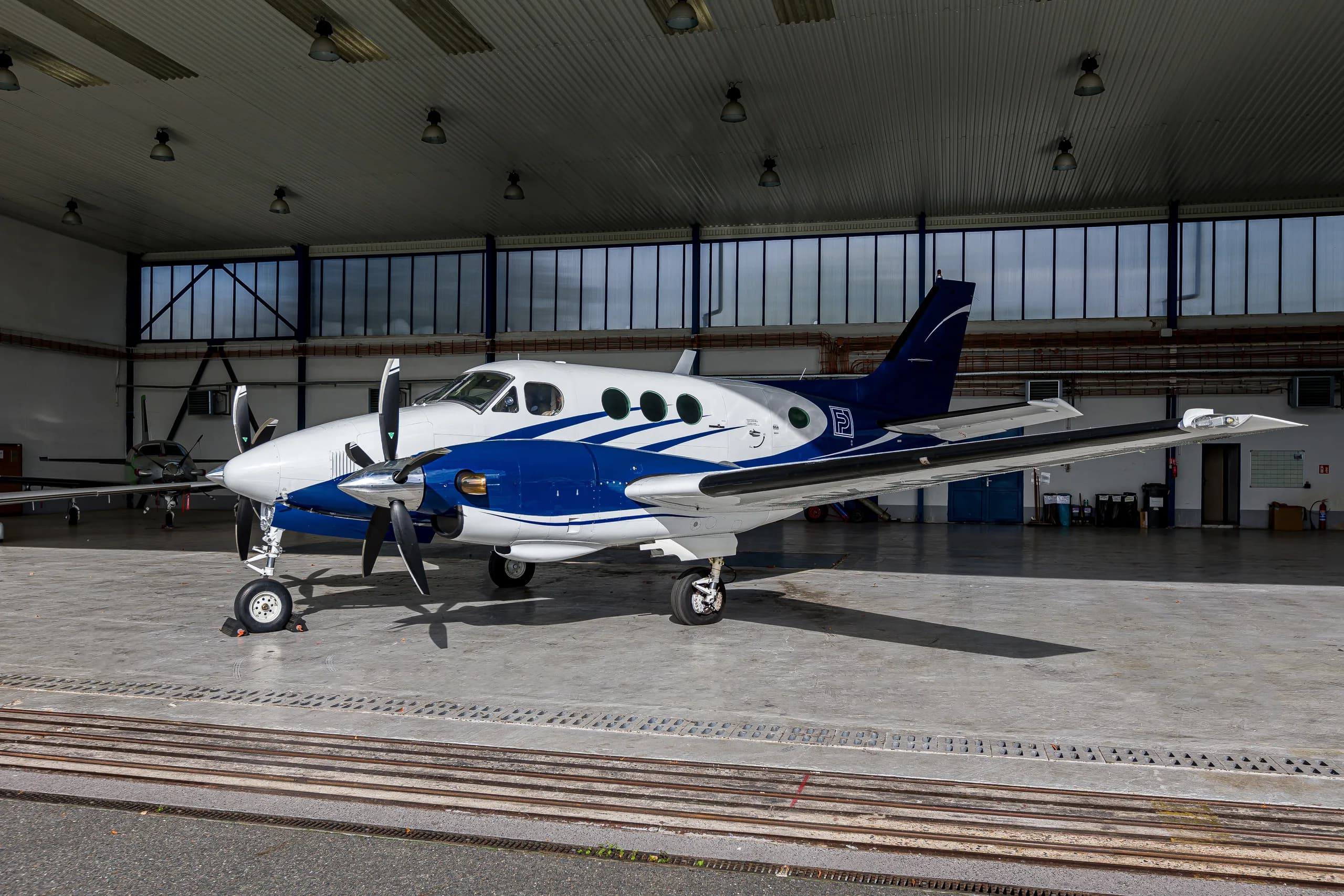 A white and blue twin-engine turboprop aircraft, likely a King Air, parked inside a hangar.