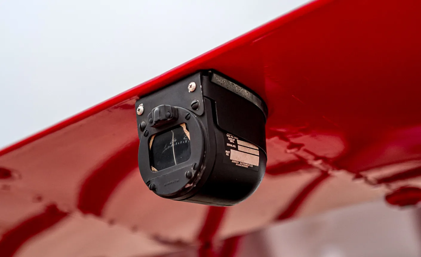 Close up of an instrument mounted on the wing of a red biplane.