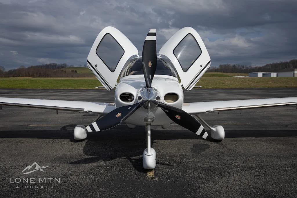 A head-on view of a white Cirrus SR22T aircraft with open doors and a three-bladed propeller.