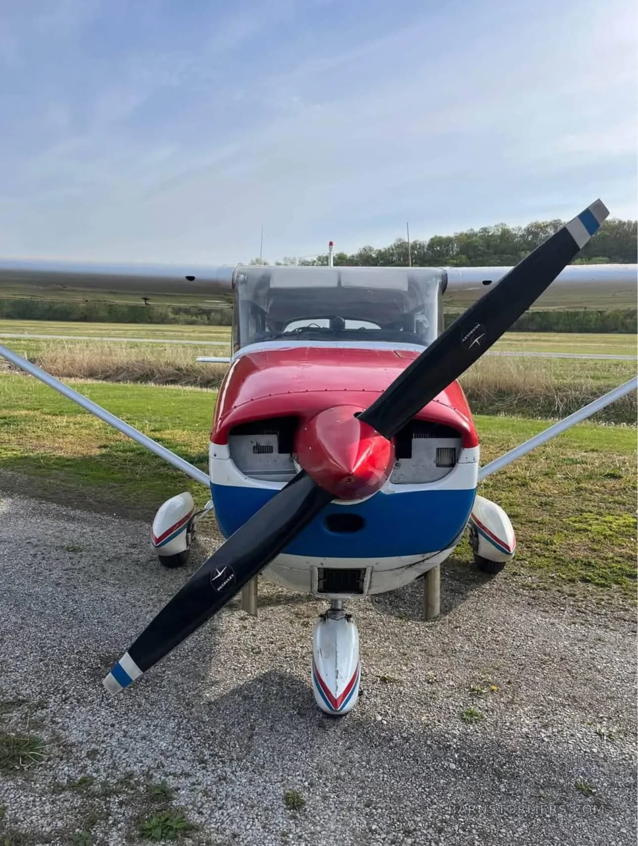 A front view of a white, red, and blue Cessna-style aircraft showing its propeller and nose cone.