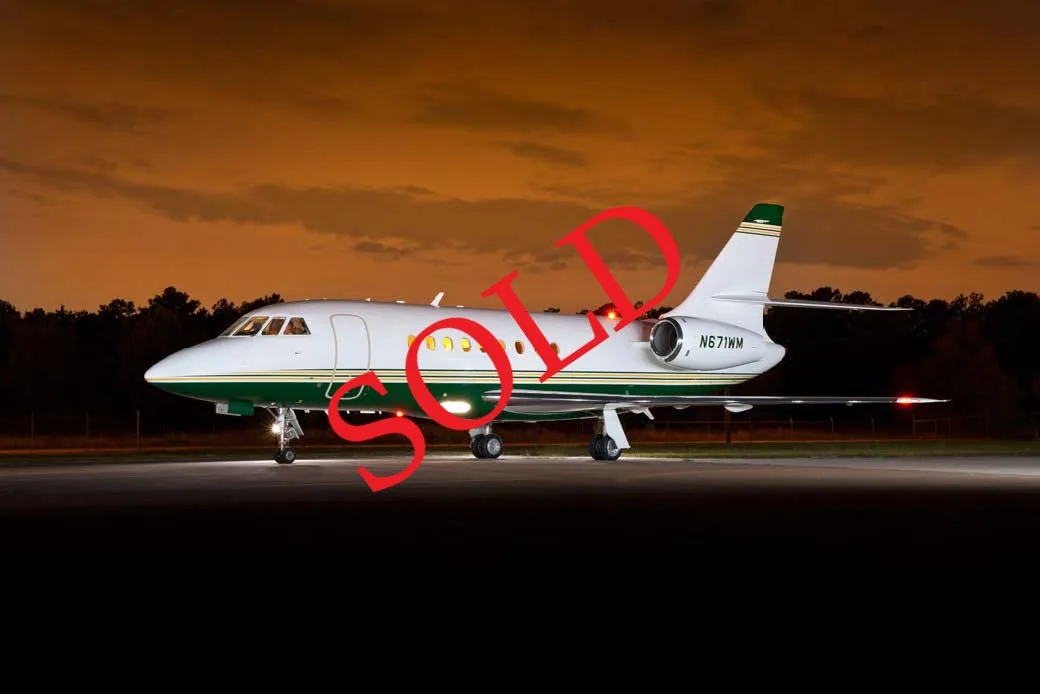 A white and green Dassault Falcon business jet with "SOLD" text, parked on an airfield at night.