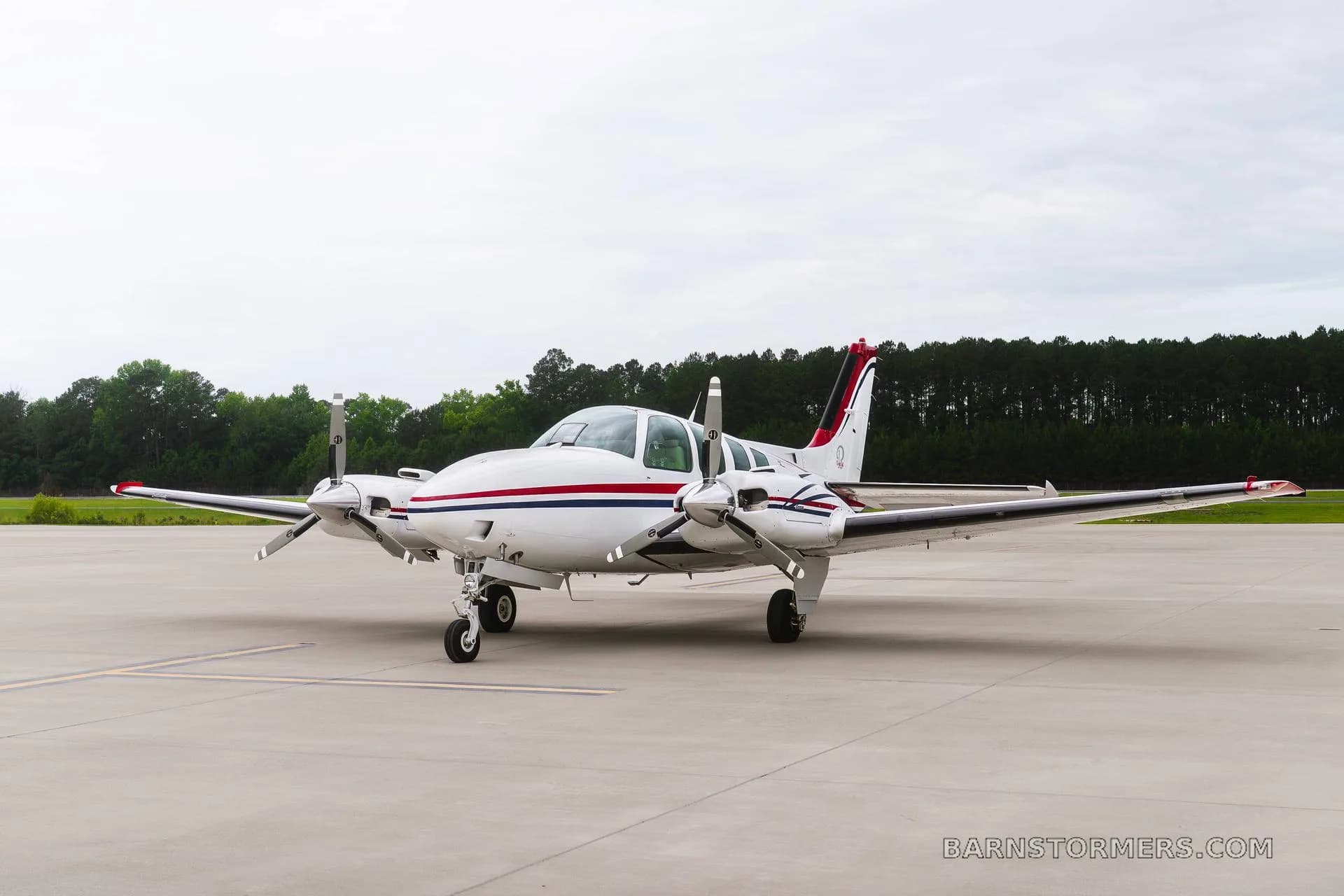 A front view of a white twin-engine propeller aircraft with red and blue stripes, registration N3194X, parked on an airfield.