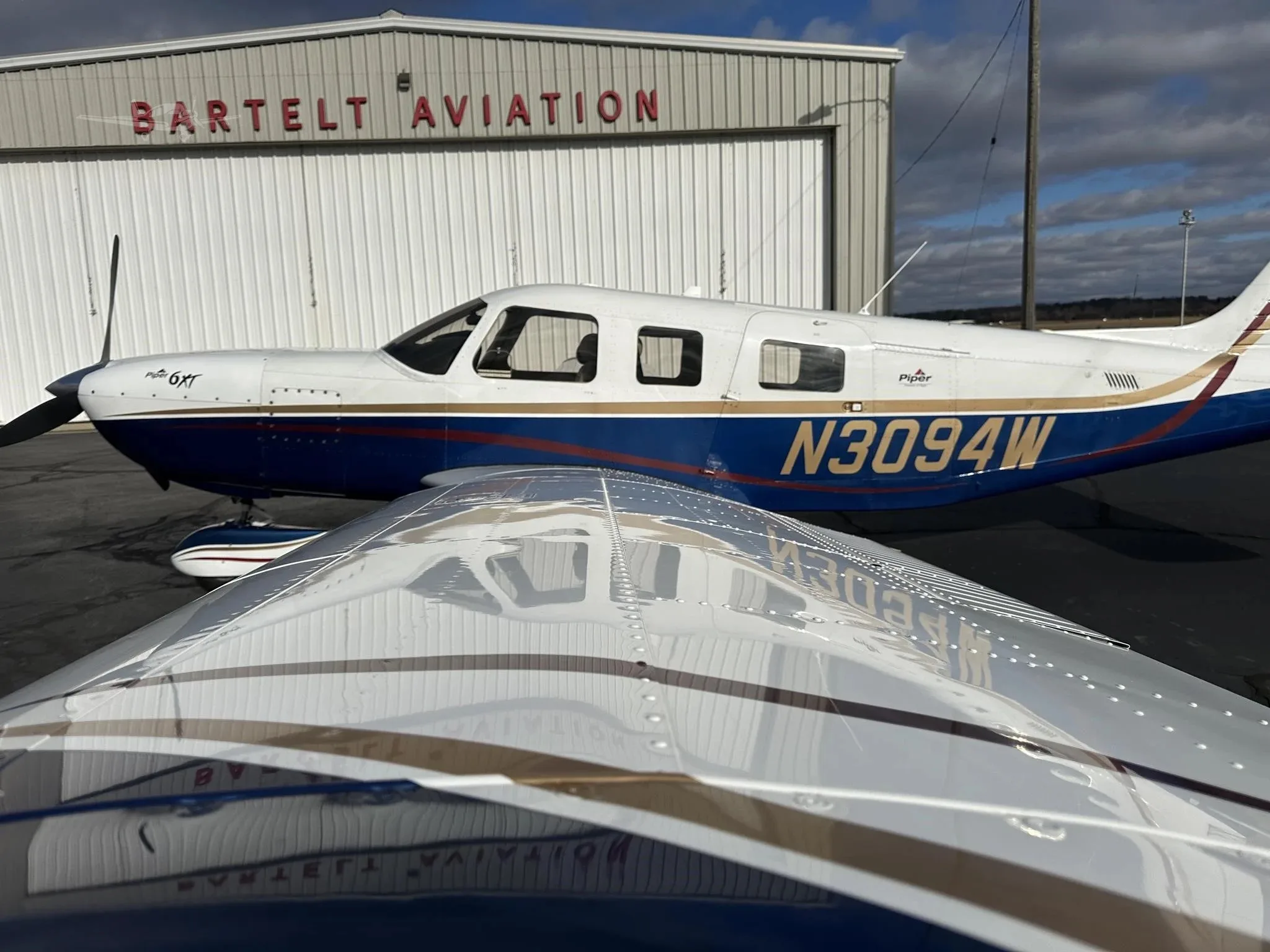 A close-up view over the wing of a blue and white Piper Malibu Mirage N3094W, showing the fuselage and propeller.