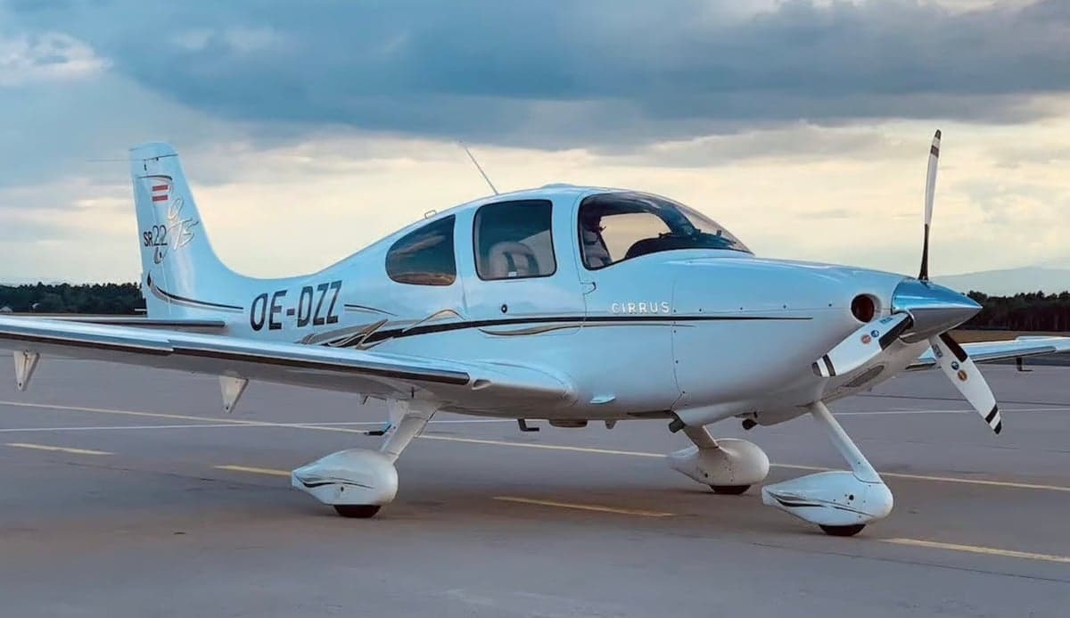 A Cirrus SR22 aircraft with registration OE-DZZ is parked on the tarmac.