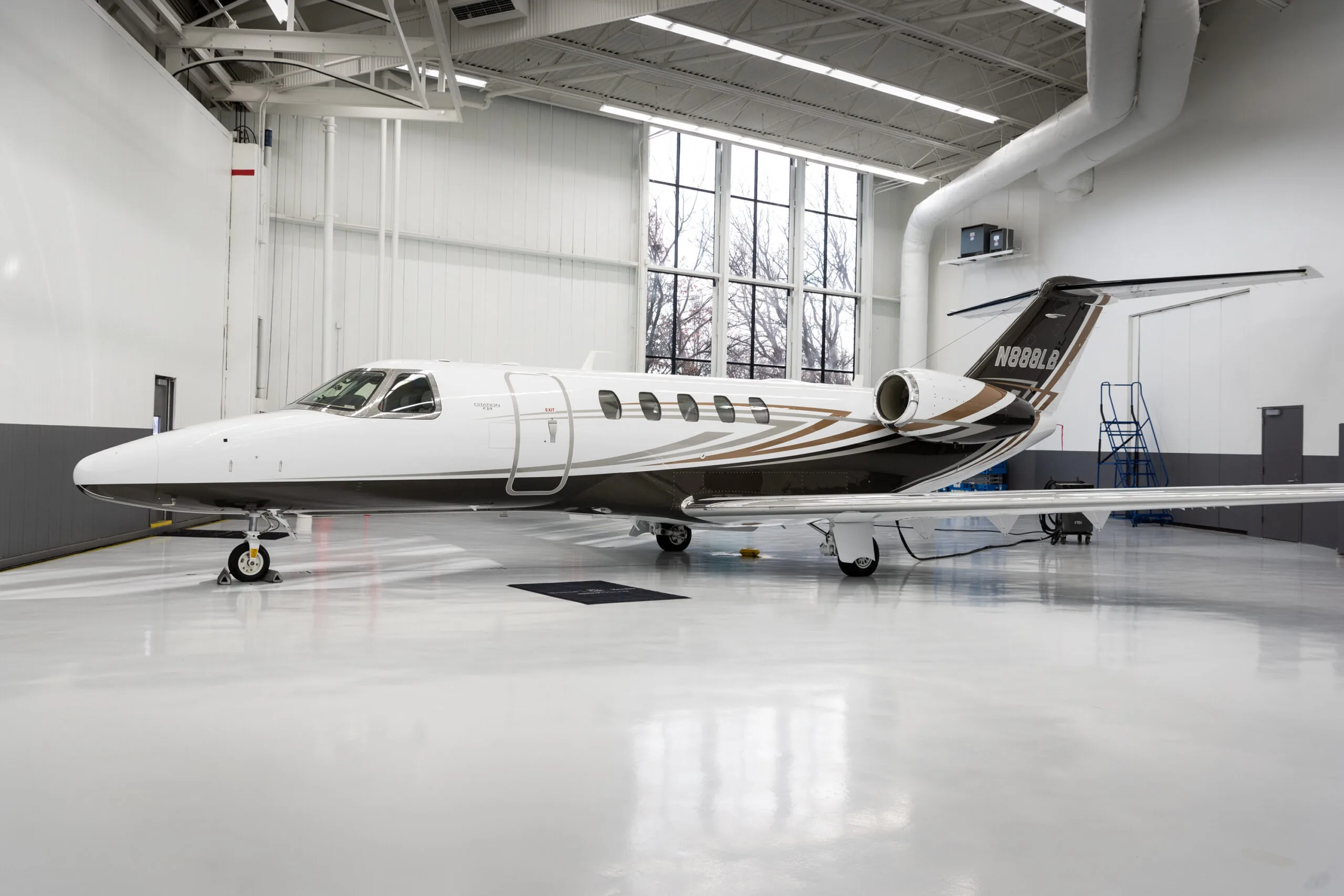 A white and brown business jet (N88LB) with a distinctive paint scheme parked in a brightly lit hangar.