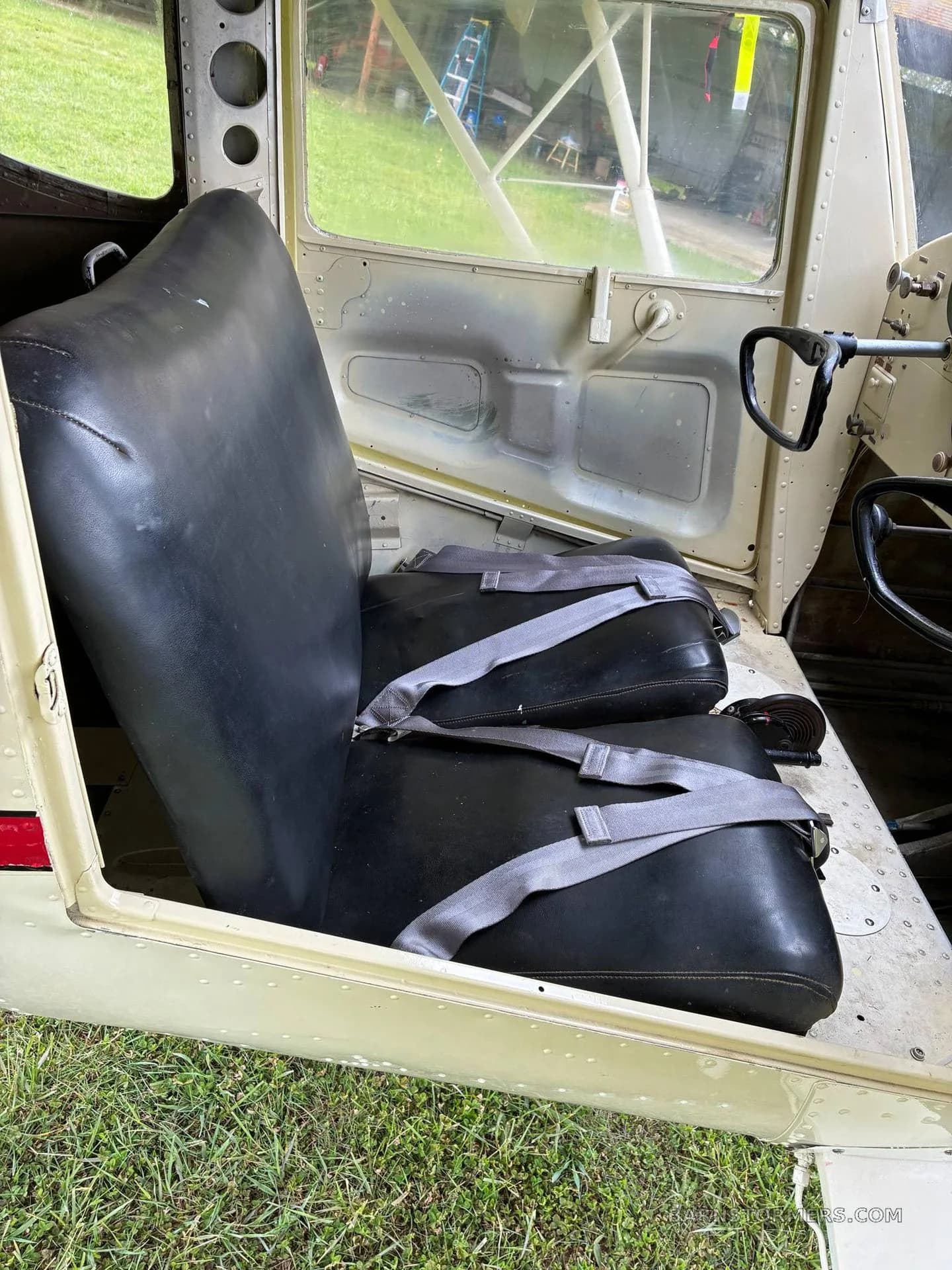 The black leather seats with grey seatbelts inside the aircraft cabin, viewed from the open door.