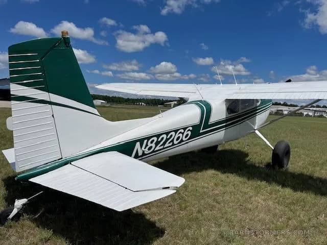 A rear-side view of a white and green single-engine propeller aircraft, registration N82266, parked on a grassy field.