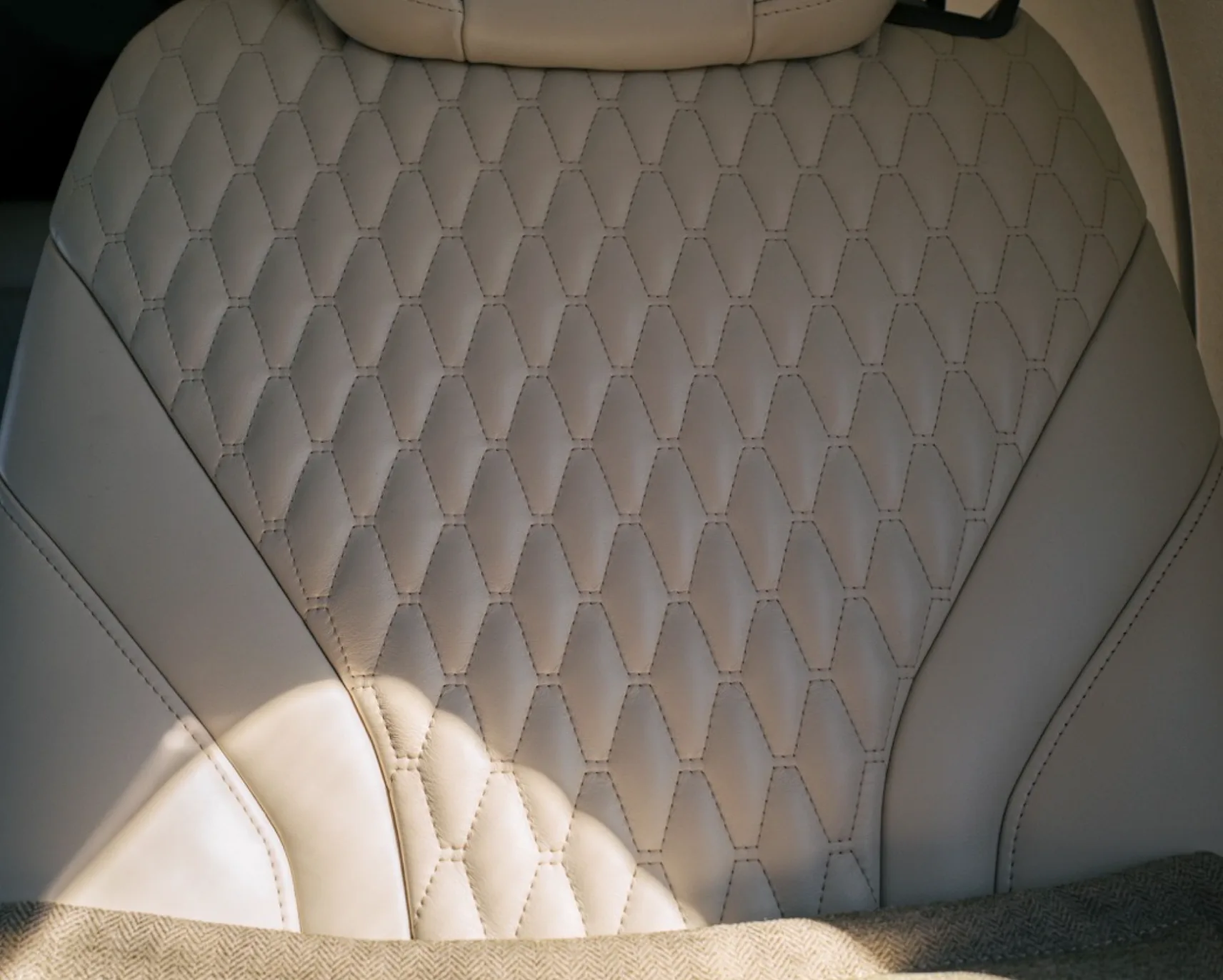 A close-up of a light-colored aircraft seat featuring a diamond-quilted pattern.