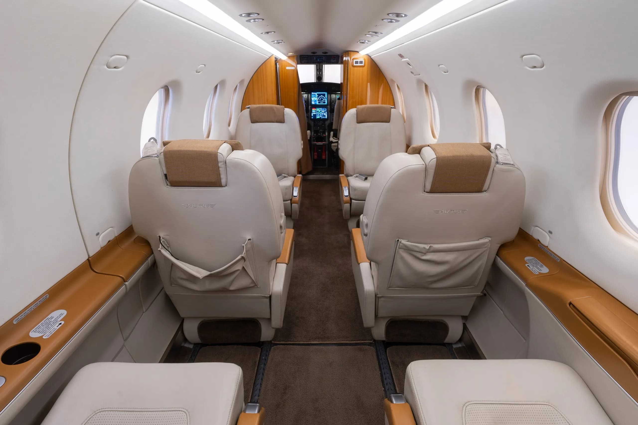 The interior cabin of the Pilatus PC-12, showing rows of beige leather seats leading towards the cockpit.