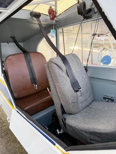 The interior of a Super Cub aircraft, showing a grey fabric front seat and a brown leather rear seat with seatbelts.