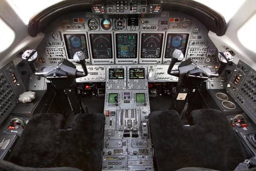 A detailed view of a modern aircraft cockpit with multiple digital displays and control yokes.