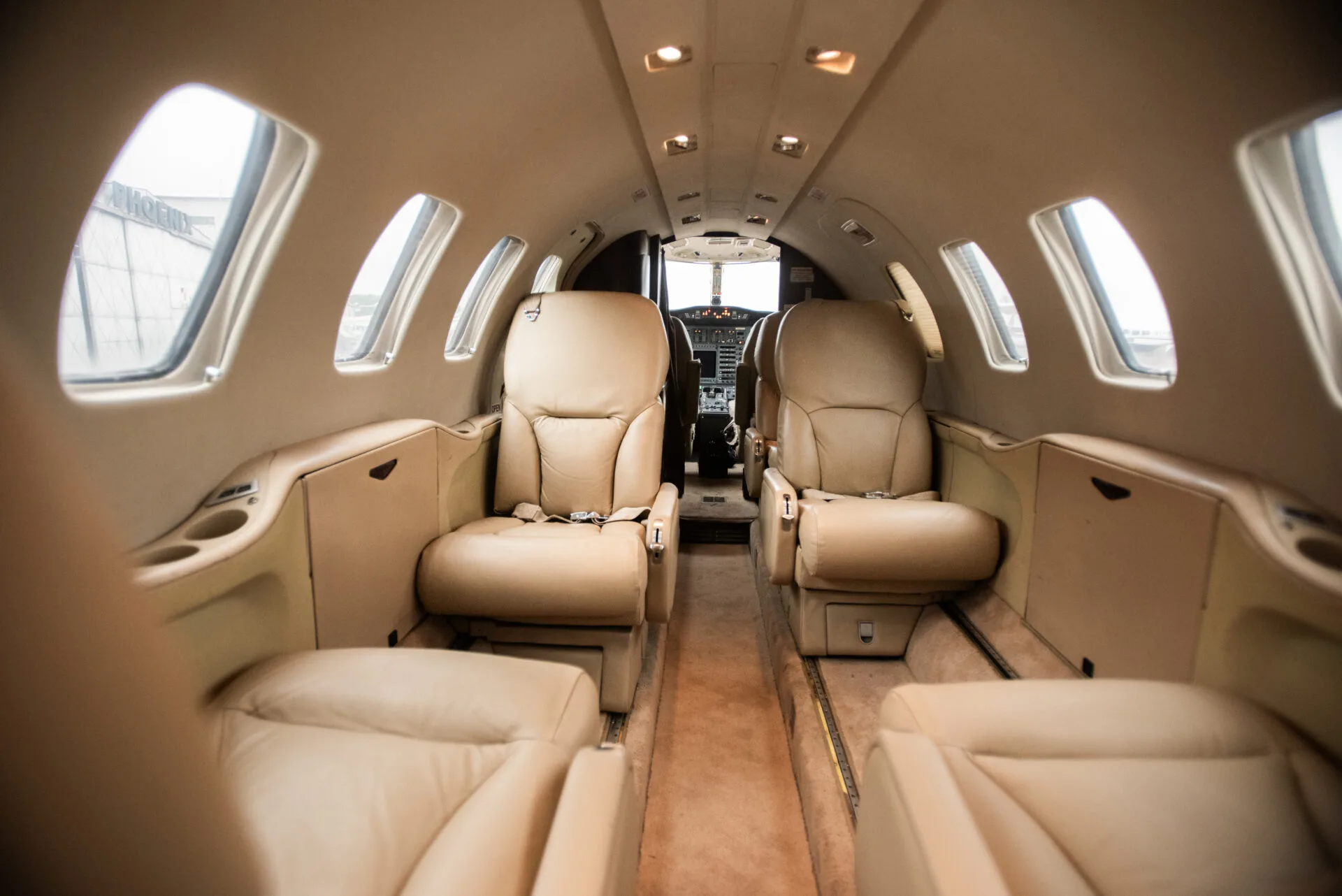The interior cabin of a business jet with tan leather seats, looking towards the cockpit.