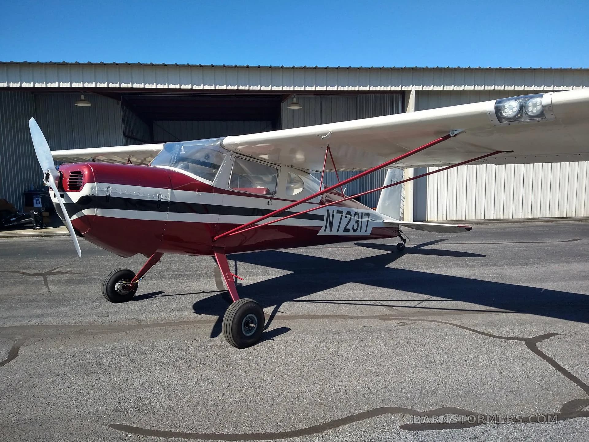 A front-side view of a red and white Cessna 140 aircraft (N72317) parked on an asphalt tarmac in front of a hangar.