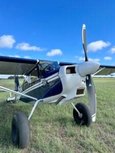 A close-up of the front of a blue and white ACA aircraft, registration N101BC, parked on a grassy field.