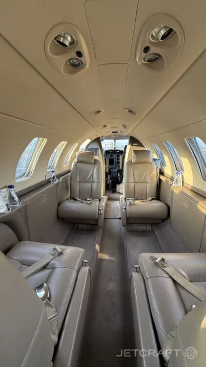The interior cabin of a private jet with light brown leather seats and a view towards the cockpit.