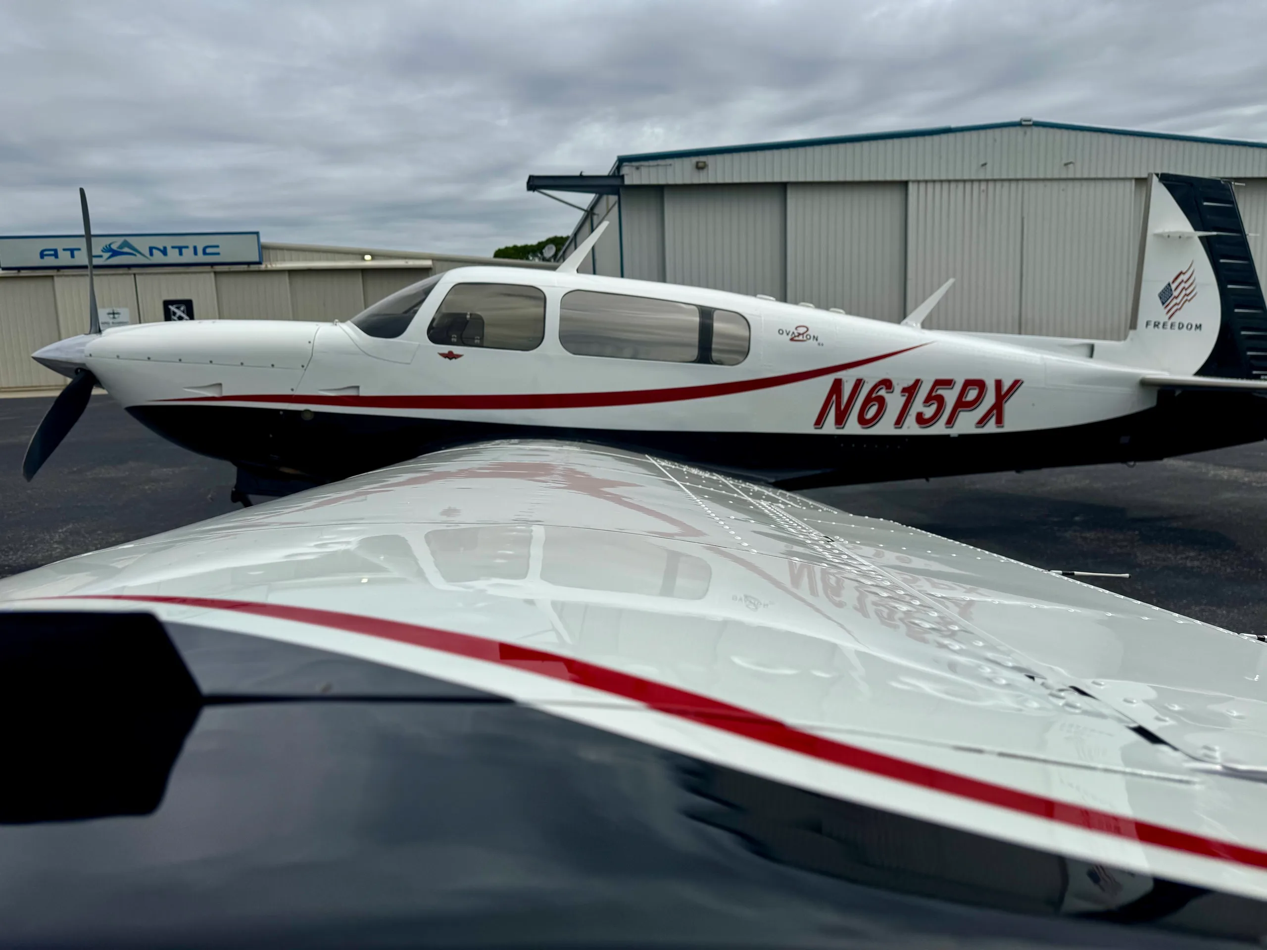 A side view of Mooney Ovation GX N615PX parked on an airfield, with a reflection of the aircraft visible on the wing.