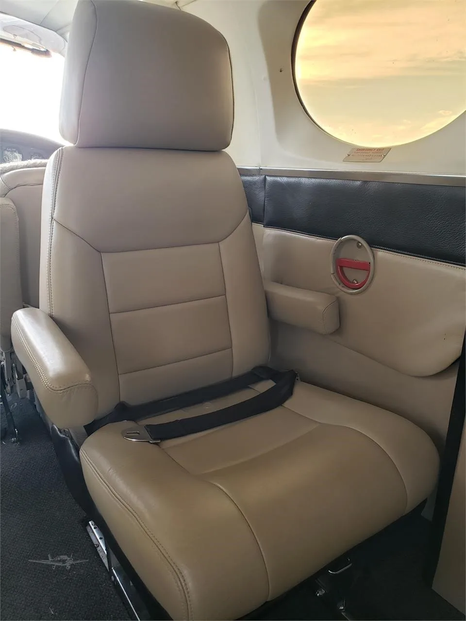 A tan leather seat with armrests and a seatbelt is shown inside the aircraft cabin.