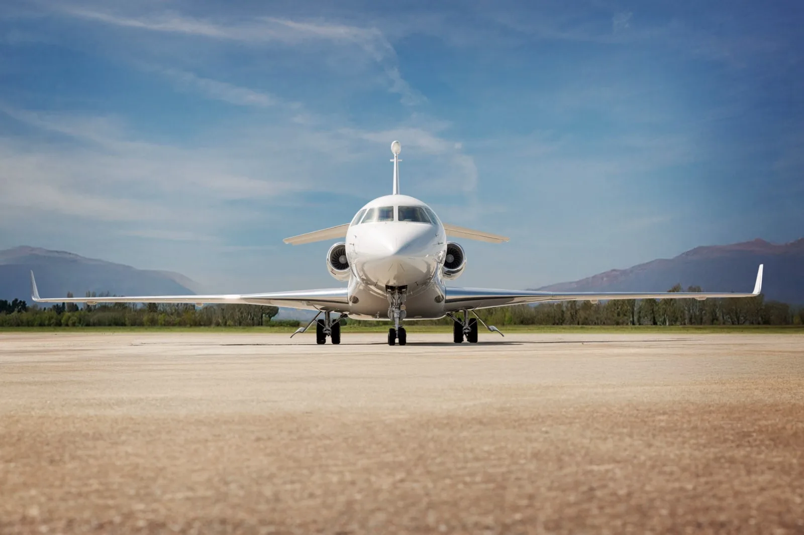 Front view of a white aircraft on the tarmac with mountains in the background.