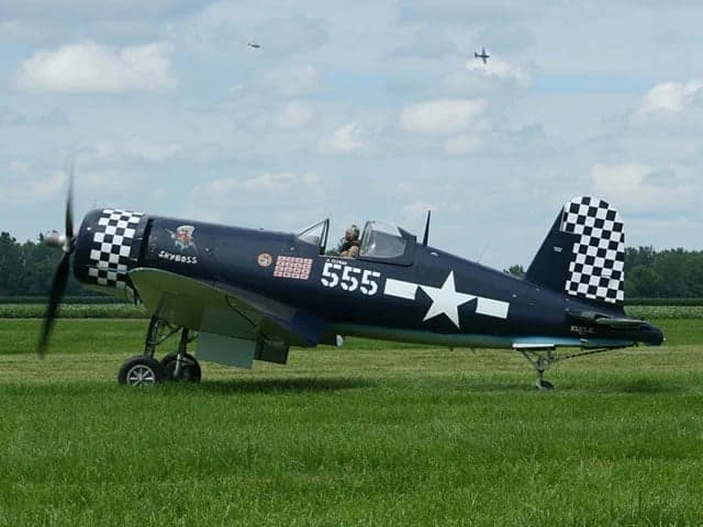 A dark blue F4U Corsair with checkerboard markings on the nose and tail, and "555" on the fuselage, on a grassy field.