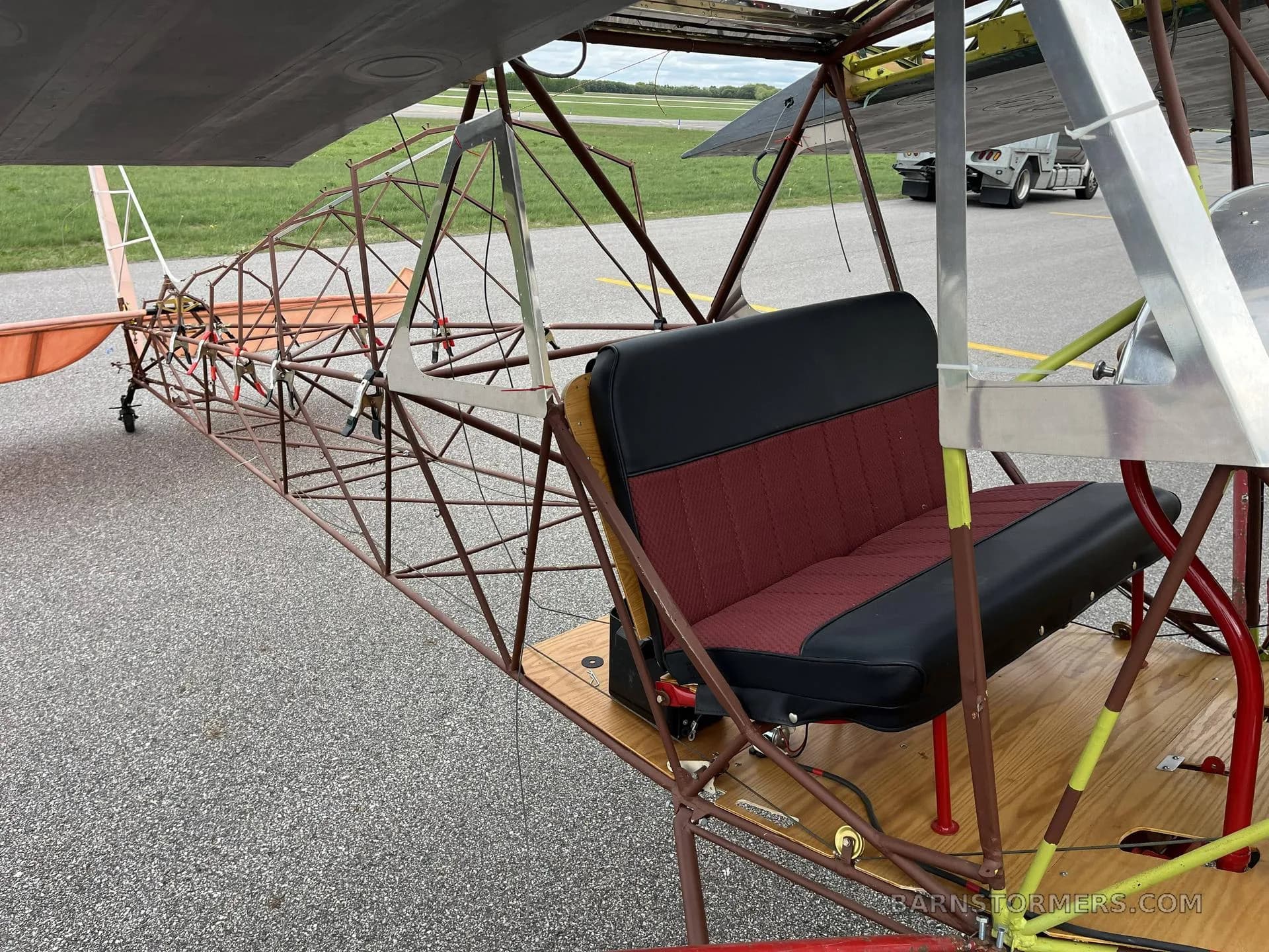A close-up of the red and black two-person bench seat and the exposed metal frame of an ultralight aircraft.