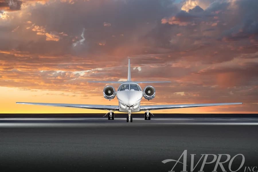 A head-on view of the white Cessna Citation Sovereign (N680FD) with blue and grey stripes, parked on a tarmac against a dramatic sunset sky.