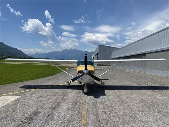 Front view of a Cessna 210 Centurion aircraft on the tarmac in front of a hangar.