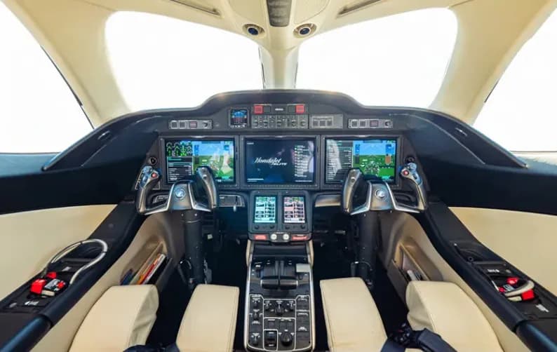 The modern cockpit of a HondaJet Elite, featuring multiple large digital displays and dual side-stick controls.