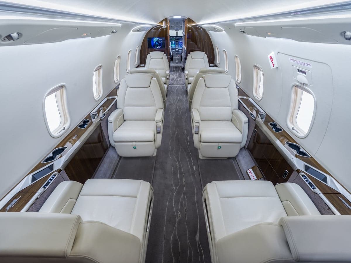 View of the aircraft's interior with white leather seats and wood trim.