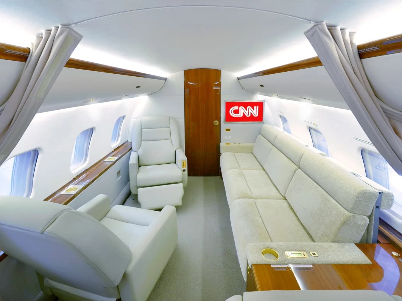 A private jet cabin with a long beige sofa on one side and individual reclining seats on the other.