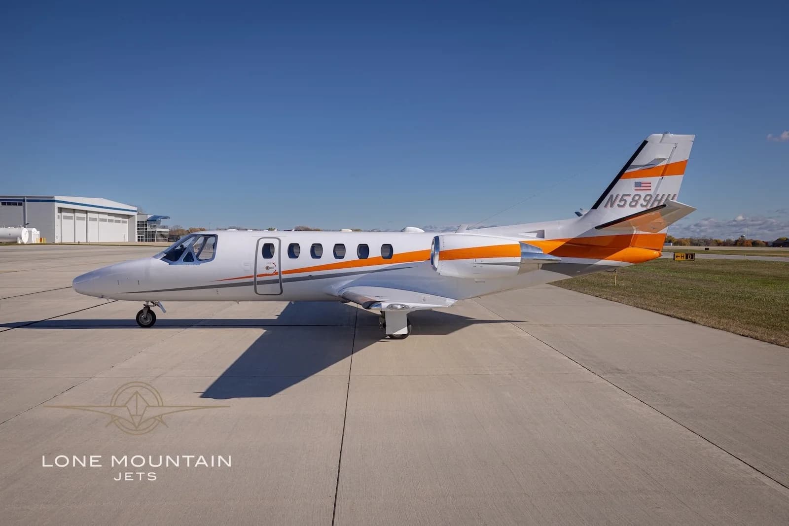 A full side view of the white Cessna Citation Bravo business jet N589HH with orange and grey stripes on the tarmac.