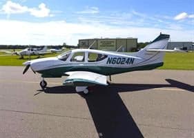 A white and green Commander 114B aircraft is parked on the tarmac.