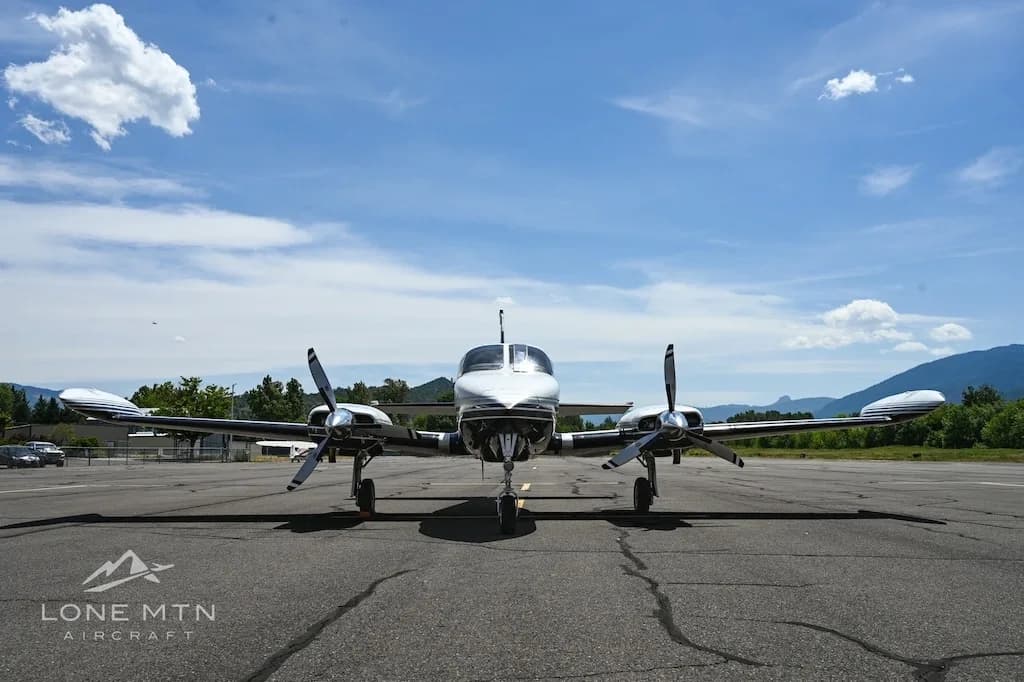 A head-on view of the white and black twin-engine aircraft, N515D, on an airfield under a blue sky.