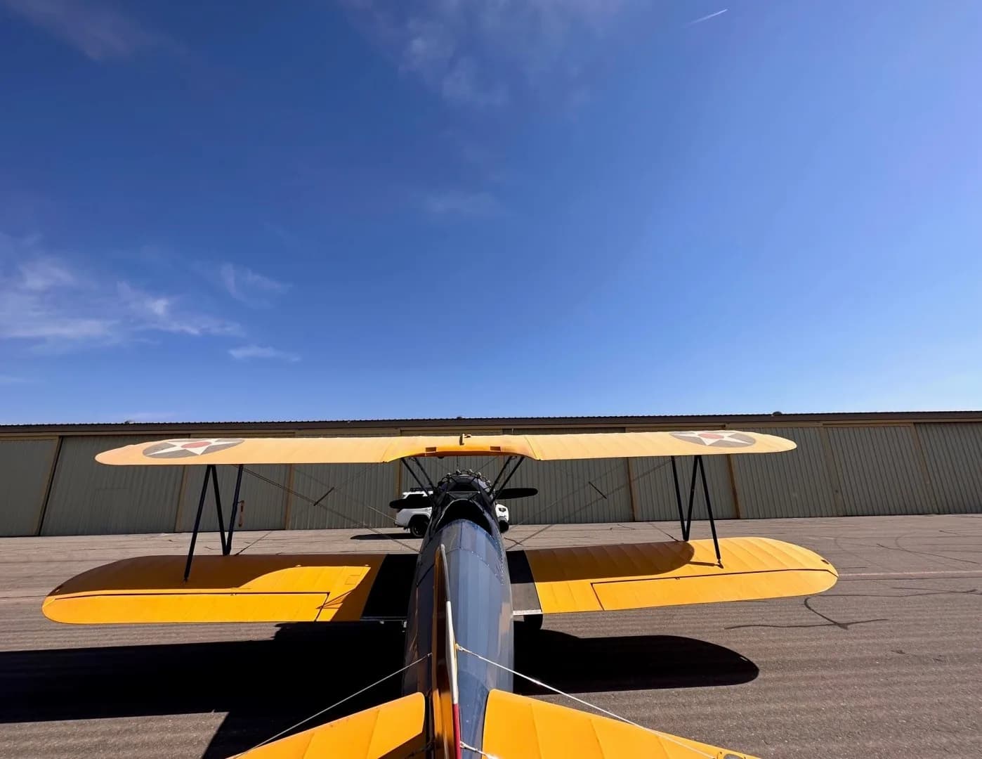 A rear view of a blue and yellow biplane with star insignia on its wings, parked on an airfield under a clear blue sky.