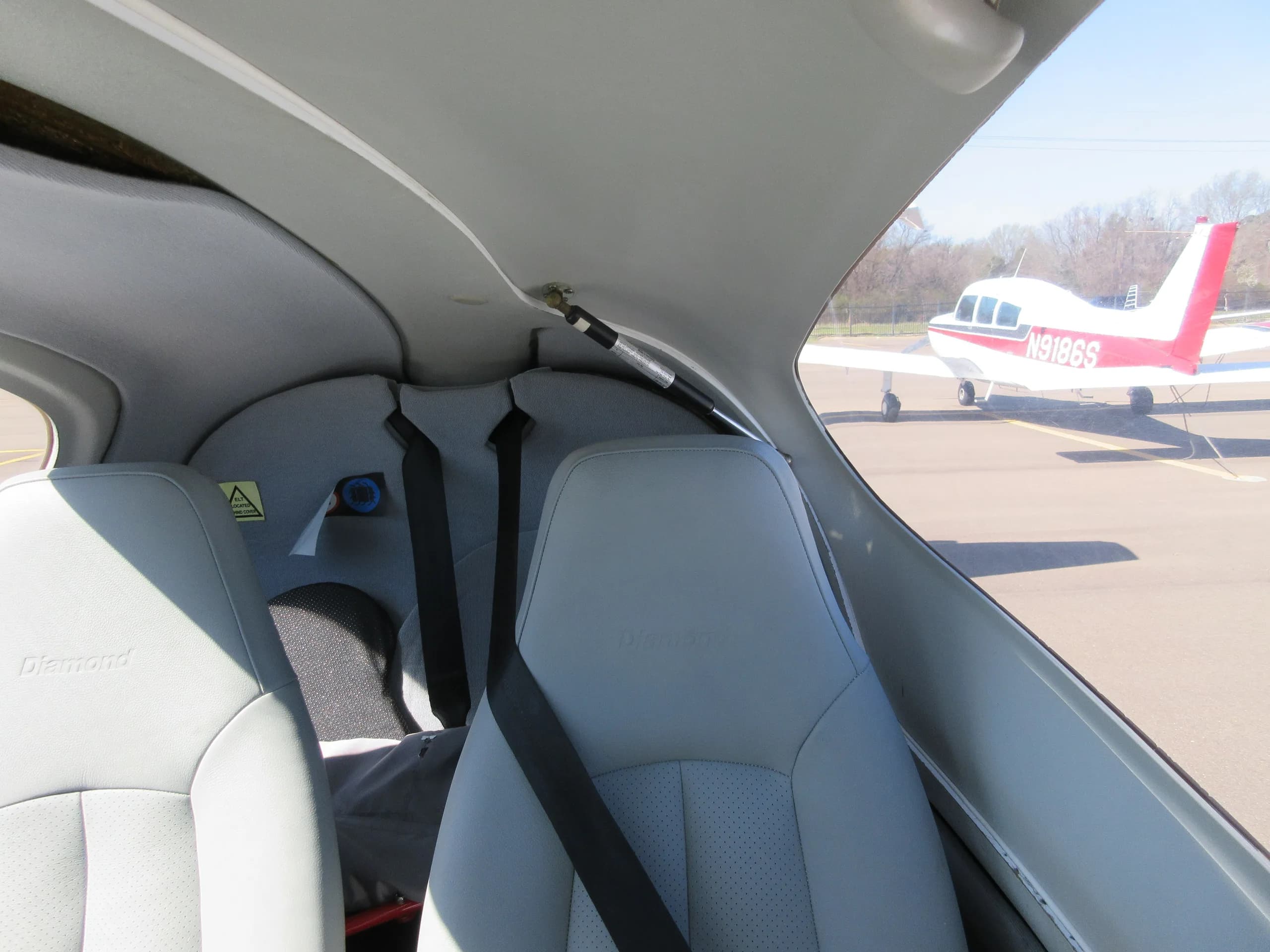 The light gray interior seats of a Diamond aircraft, viewed from the cockpit looking back, with another aircraft visible outside.