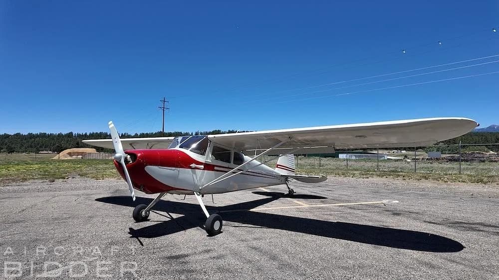 A red and white 1950 Cessna 170A aircraft parked on an asphalt surface under a clear blue sky.