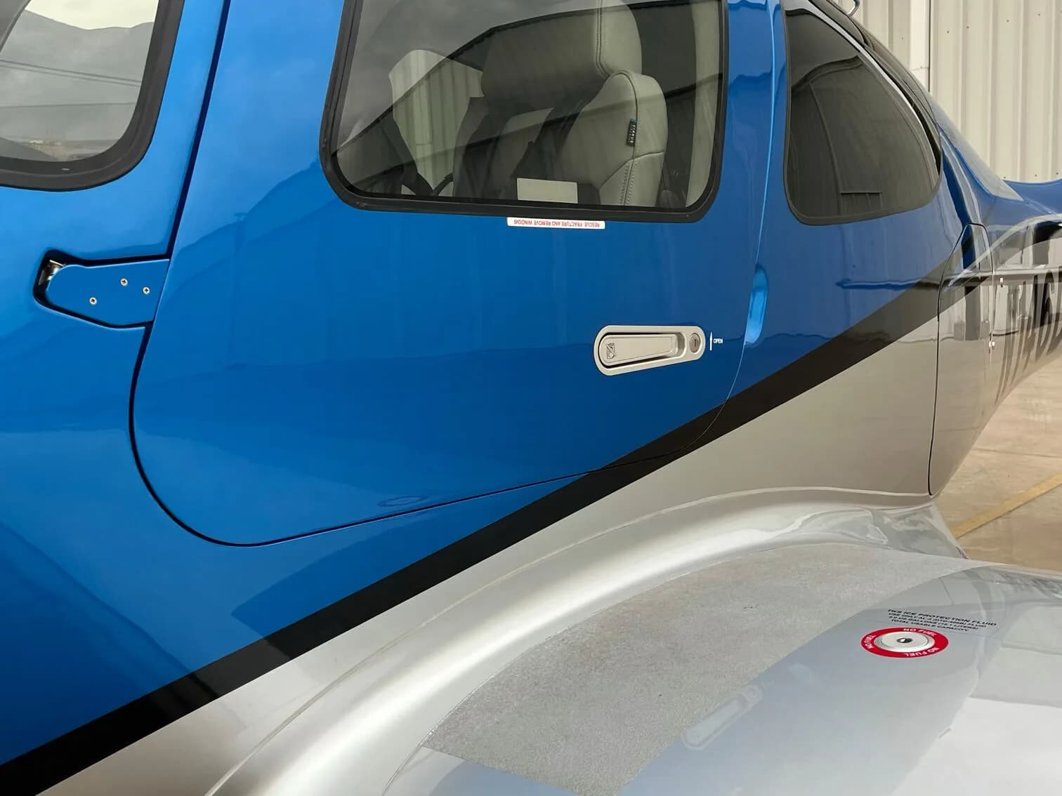 A close-up of the cockpit door and fuselage of the blue and silver Cirrus SR22 GTS aircraft.