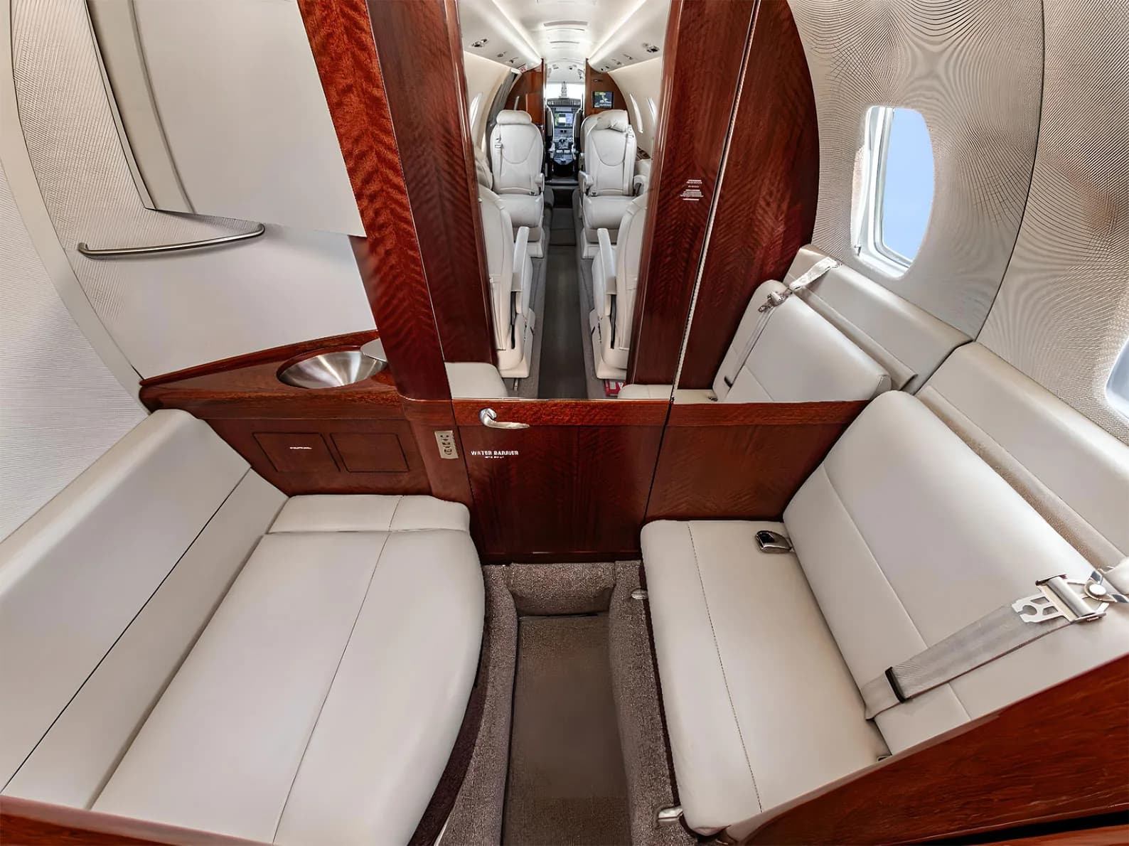 The rear section of a private jet cabin with two opposing light leather divan seats and dark wood cabinetry.