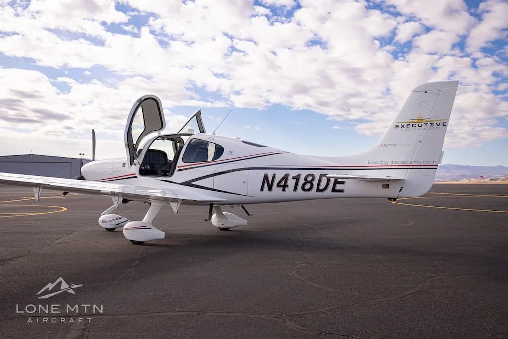A white Cirrus SR22 aircraft with black and red stripes, registration N418DE, parked on an airfield with doors open.