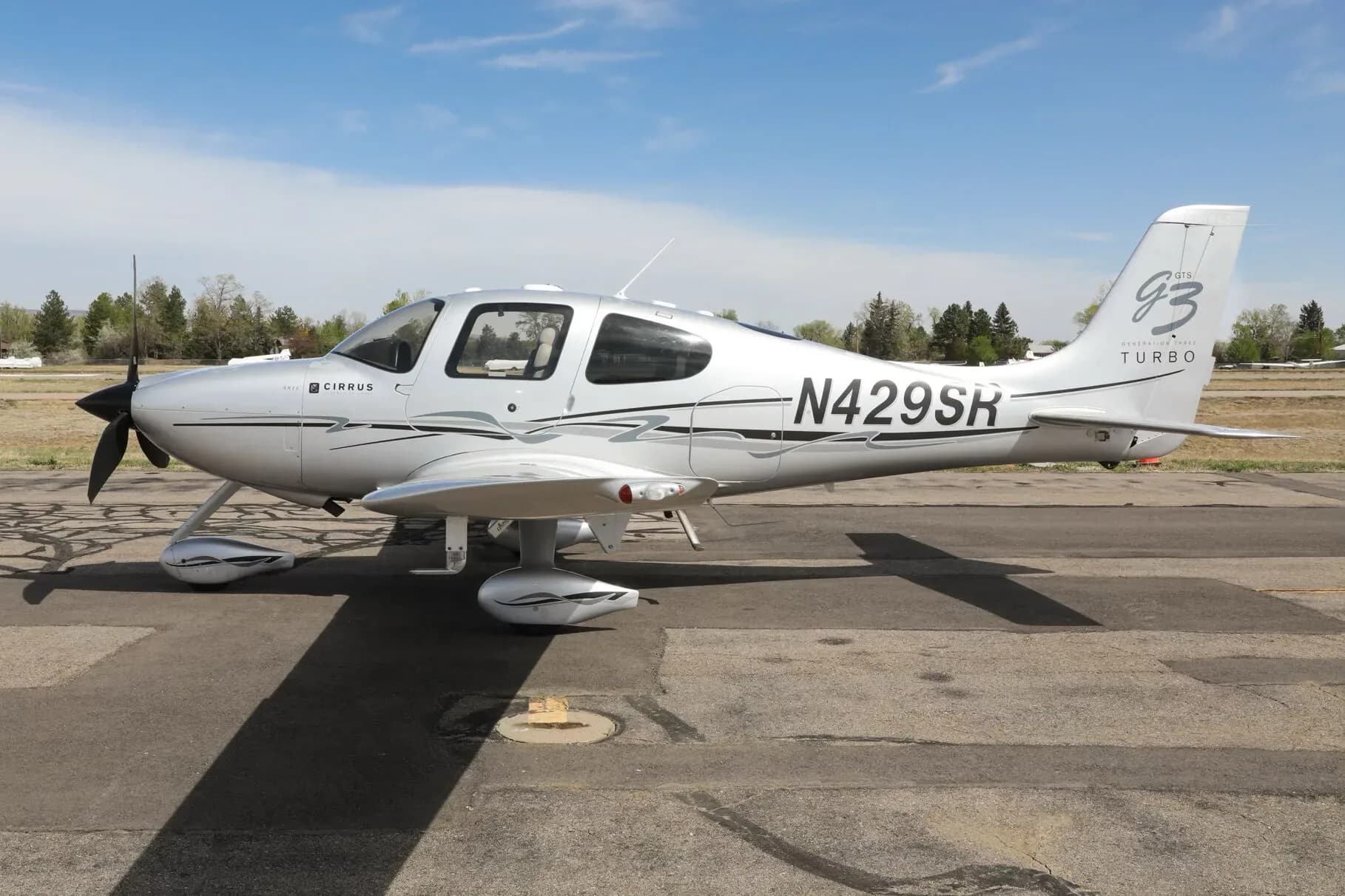 A silver Cirrus SR22T aircraft with black and grey accents, registration N429SR, parked on an asphalt ramp under a blue sky.