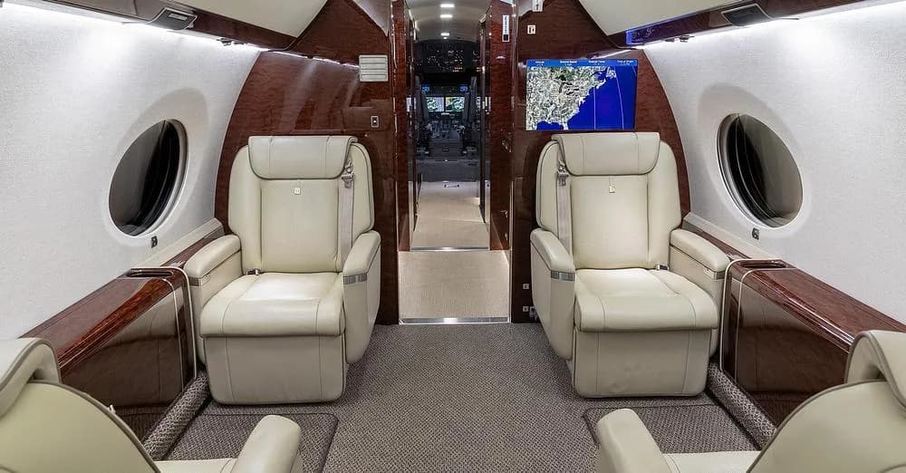The Gulfstream G650 cabin interior with two facing light leather seats and a large map display screen.