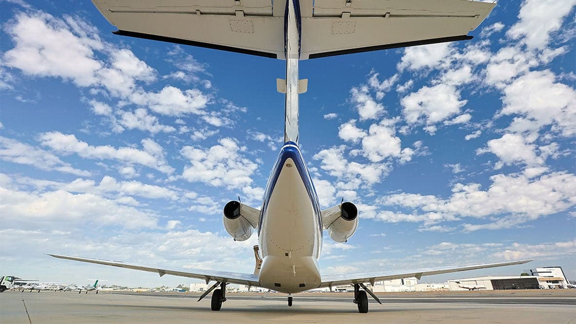 A rear view of a white and blue Cessna Citation CJ1 aircraft with registration N9915Z parked on the tarmac with a cloudy sky overhead.